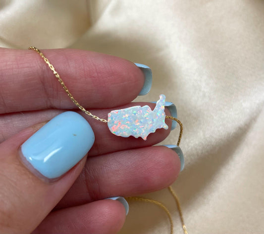 A hand holding a USA map-shaped pendant necklace with opal stones in blue and white colors.