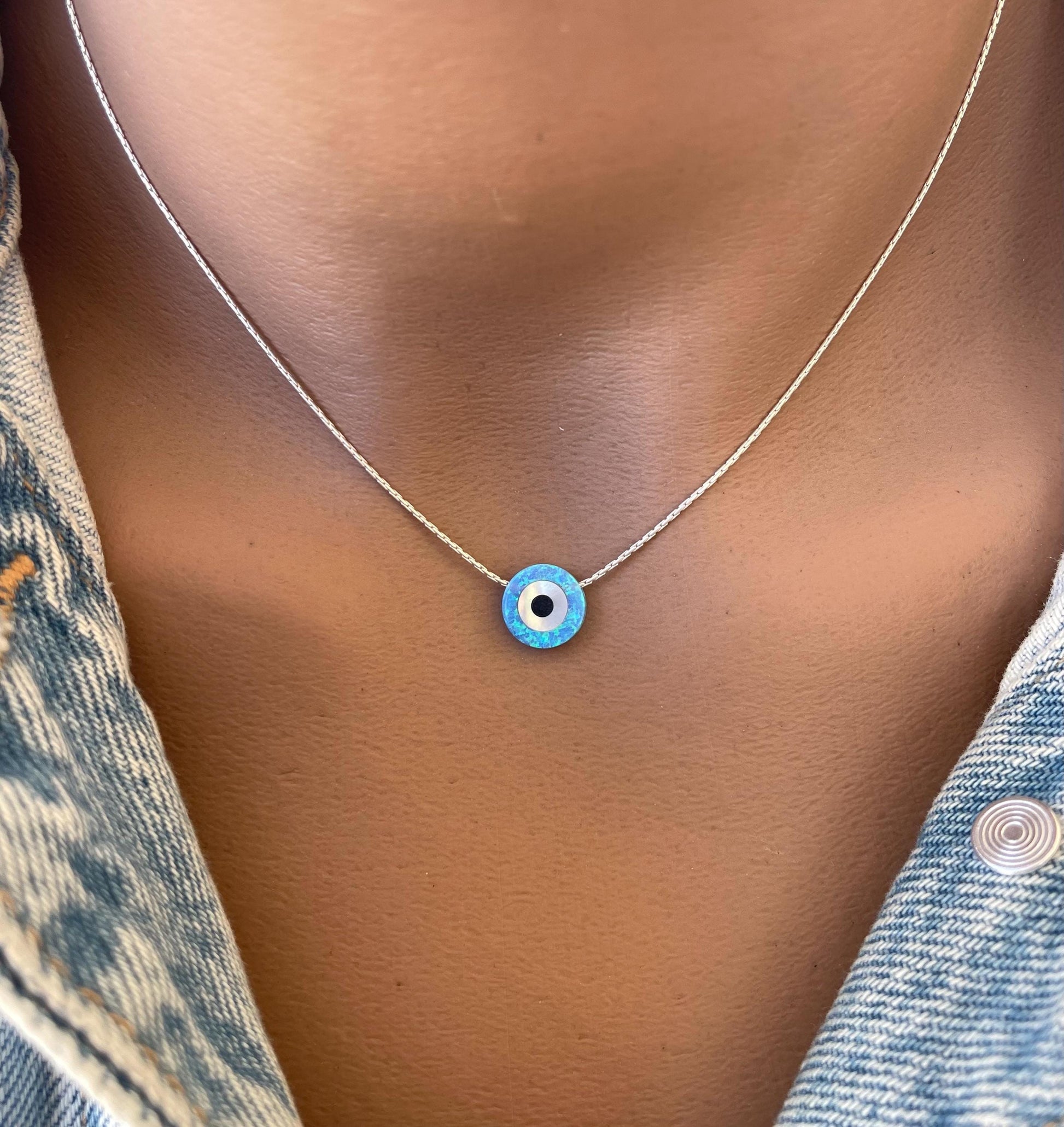 A close-up image of a person wearing a necklace with a blue lab opal coin pendant, representing the evil eye symbol.