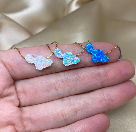 A collection of Hawaiian opal necklaces with pendant shapes representing different islands, displayed on a person's hand.