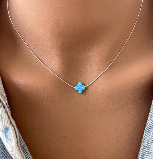 A person wearing a blue and white opal clover pendant necklace on a close-up of the neck.