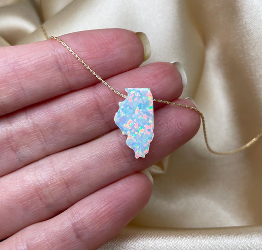 An Illinois-shaped opal pendant necklace held in a person's hand, with the shiny surface of the opal reflecting light.