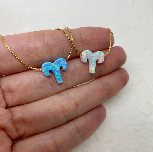 Two Aries zodiac charm necklaces with opal stones, one on a gold-filled chain and the other on a silver chain, laid on a hand.
