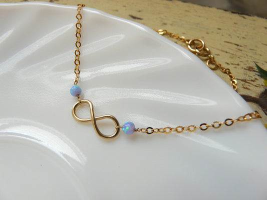 A gold-filled infinity charm bracelet with wire-wrapped tiny opal beads displayed on a white surface.
