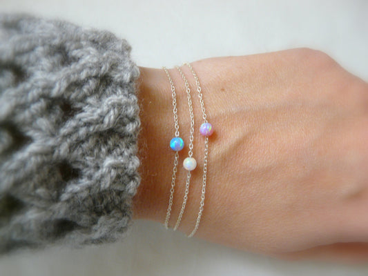 A delicate opal bracelet with a 4mm opal bead, showcased on a person's wrist, with the beads reflecting colorful light.