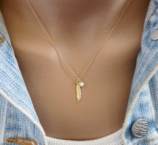 A gold-filled feather charm necklace with an opal-pearl bead, displayed on a model wearing a denim jacket.