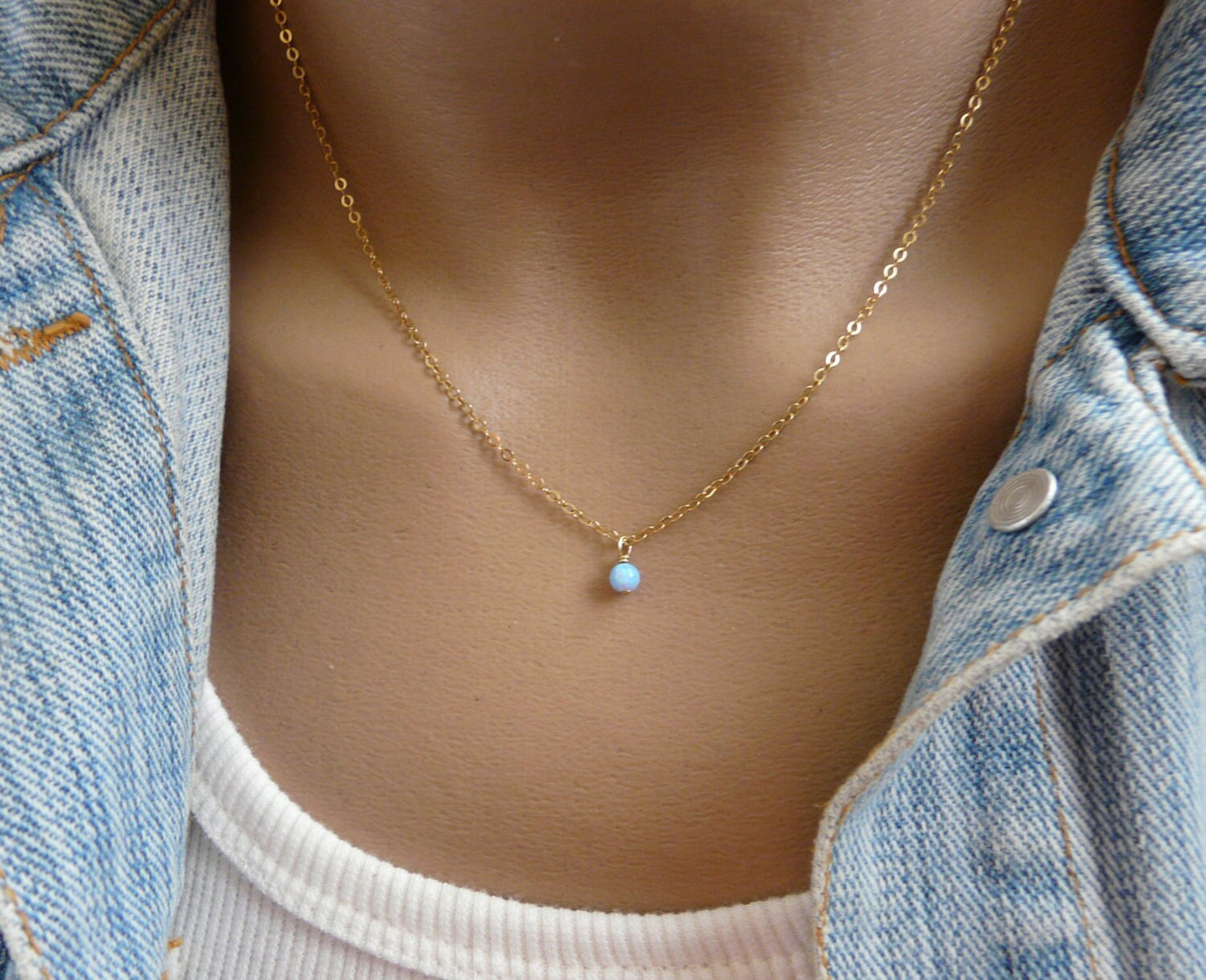 A person wearing a minimalist opal bead necklace in gold color, displayed against a casual outfit background.