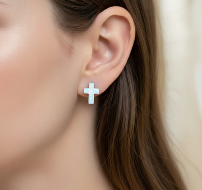 Close-up of an ear wearing a silver cross earring with a blurred background