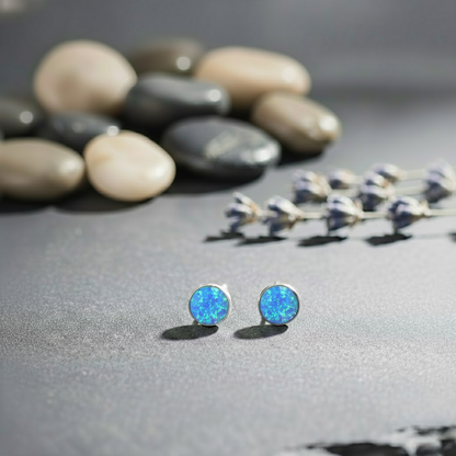 Blue opal stud earrings on a gray surface with pebbles and lavender in the background