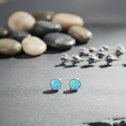 Opal stud earrings on a gray surface with pebbles and dried flowers in the background