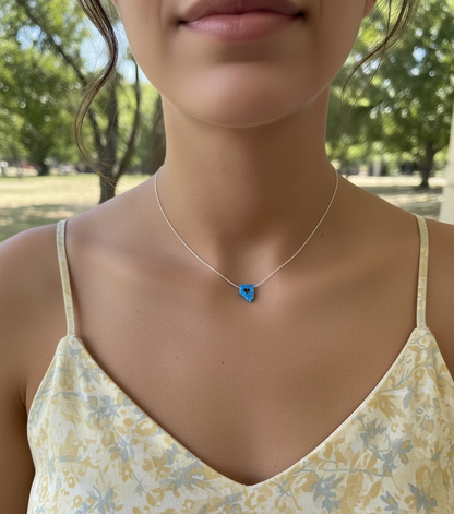 Necklace with a blue heart pendant worn by a person in a floral dress outdoors.