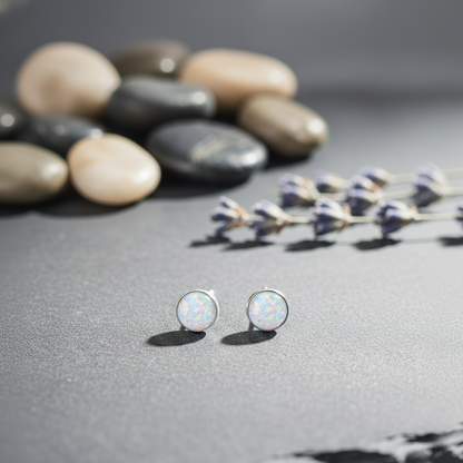 Opal stud earrings on a gray surface with stones and dried lavender.