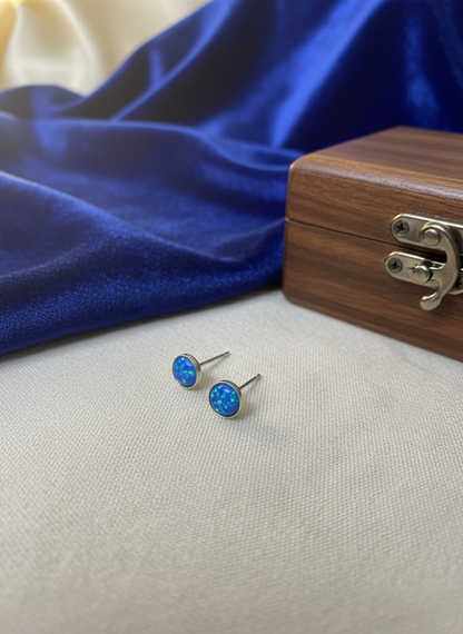 Blue opal stud earrings on a white surface with a wooden box in the background