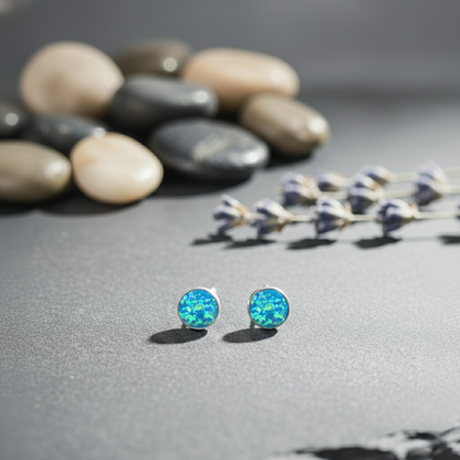 Blue opal stud earrings on a gray surface with pebbles and lavender in the background