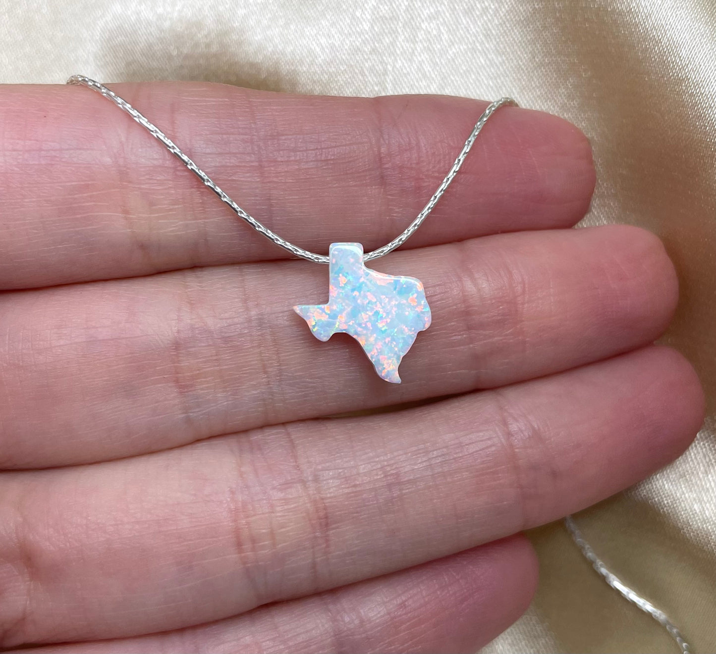 Silver necklace with a Texas-shaped pendant held between fingers on a beige background