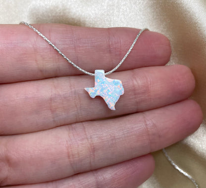 Silver necklace with a Texas-shaped pendant held between fingers on a beige background