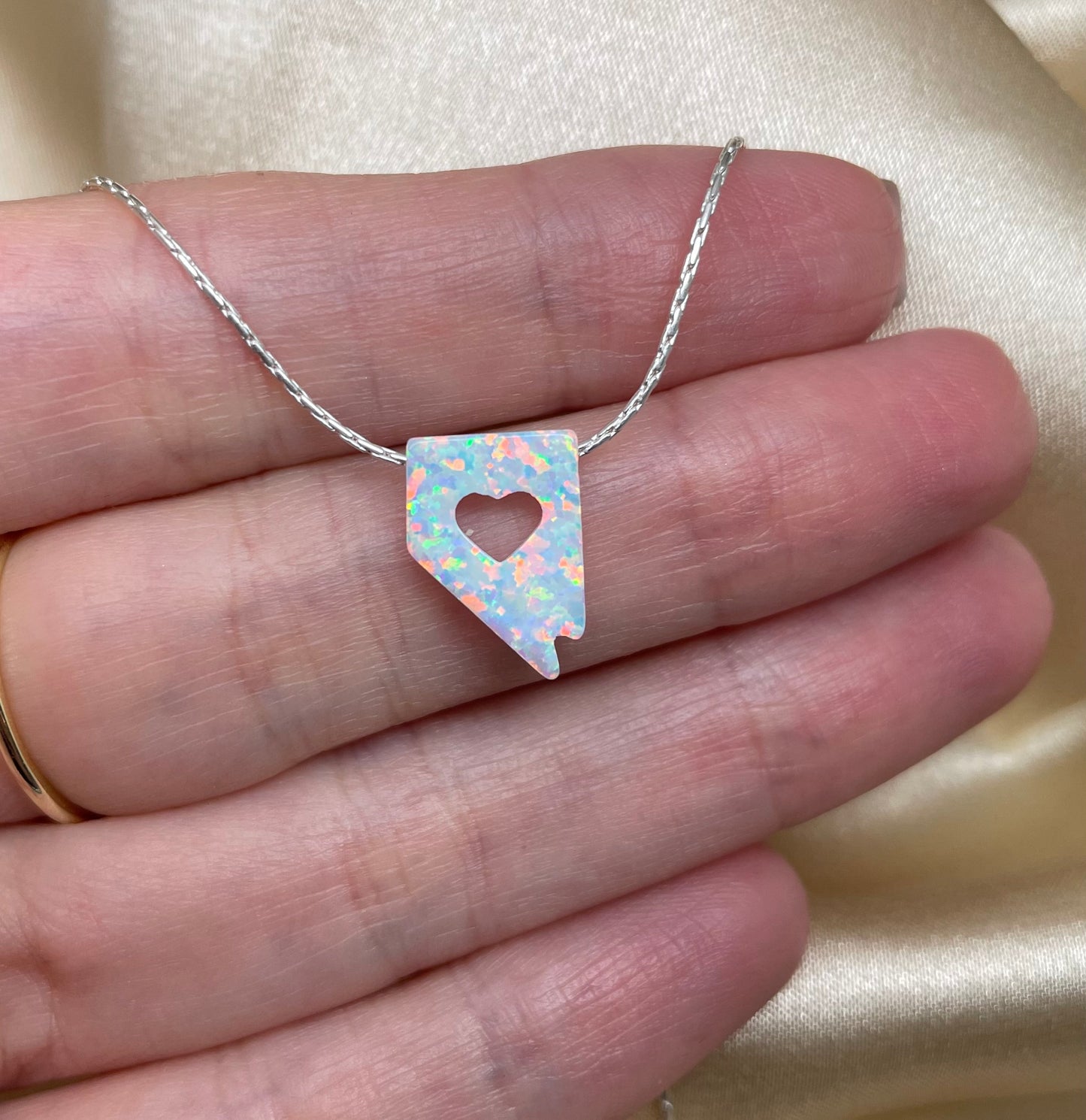 Necklace with a multicolored heart-shaped pendant held between fingers on a neutral background