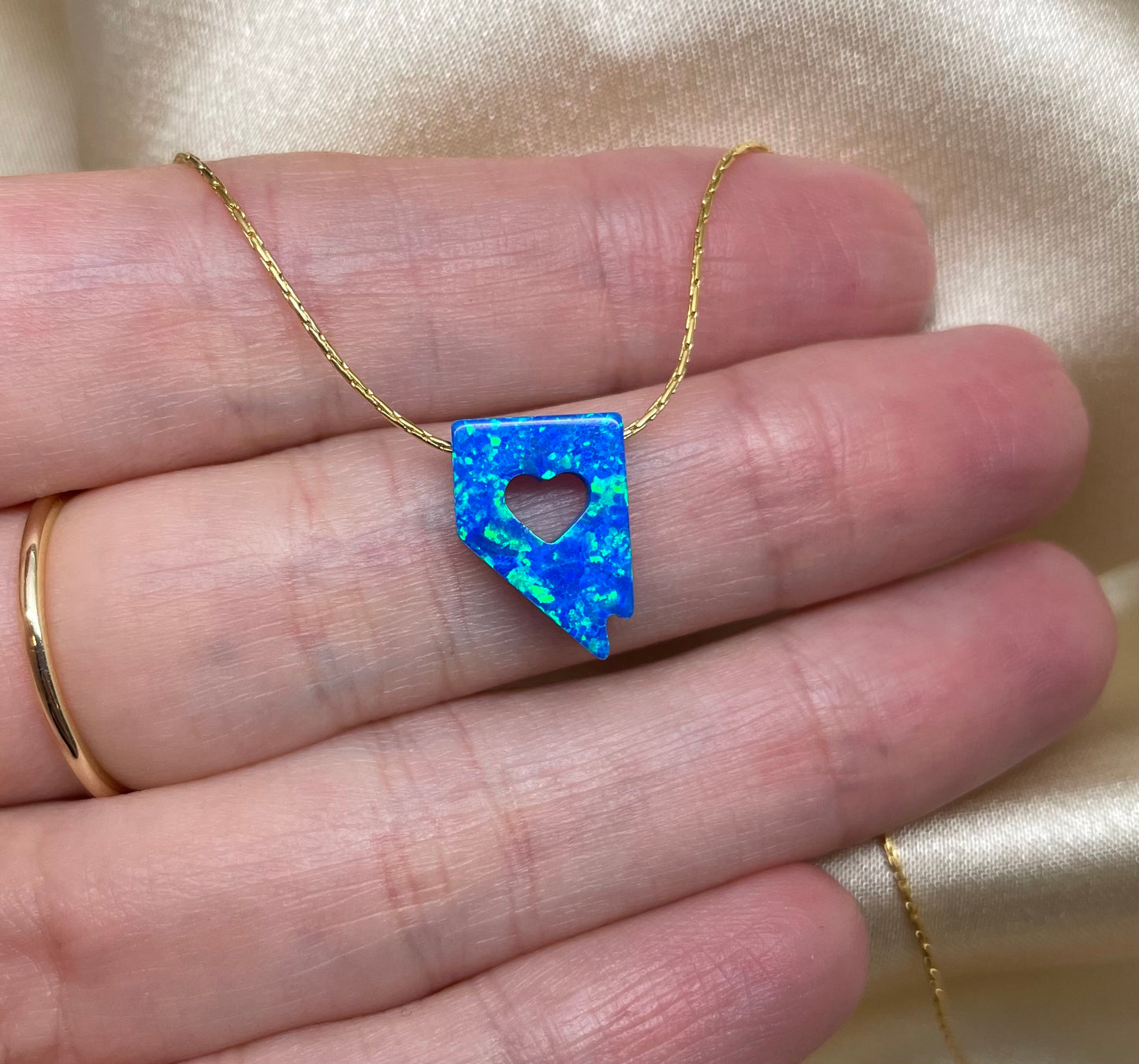 Blue opal necklace with heart cutout held between fingers against a beige background
