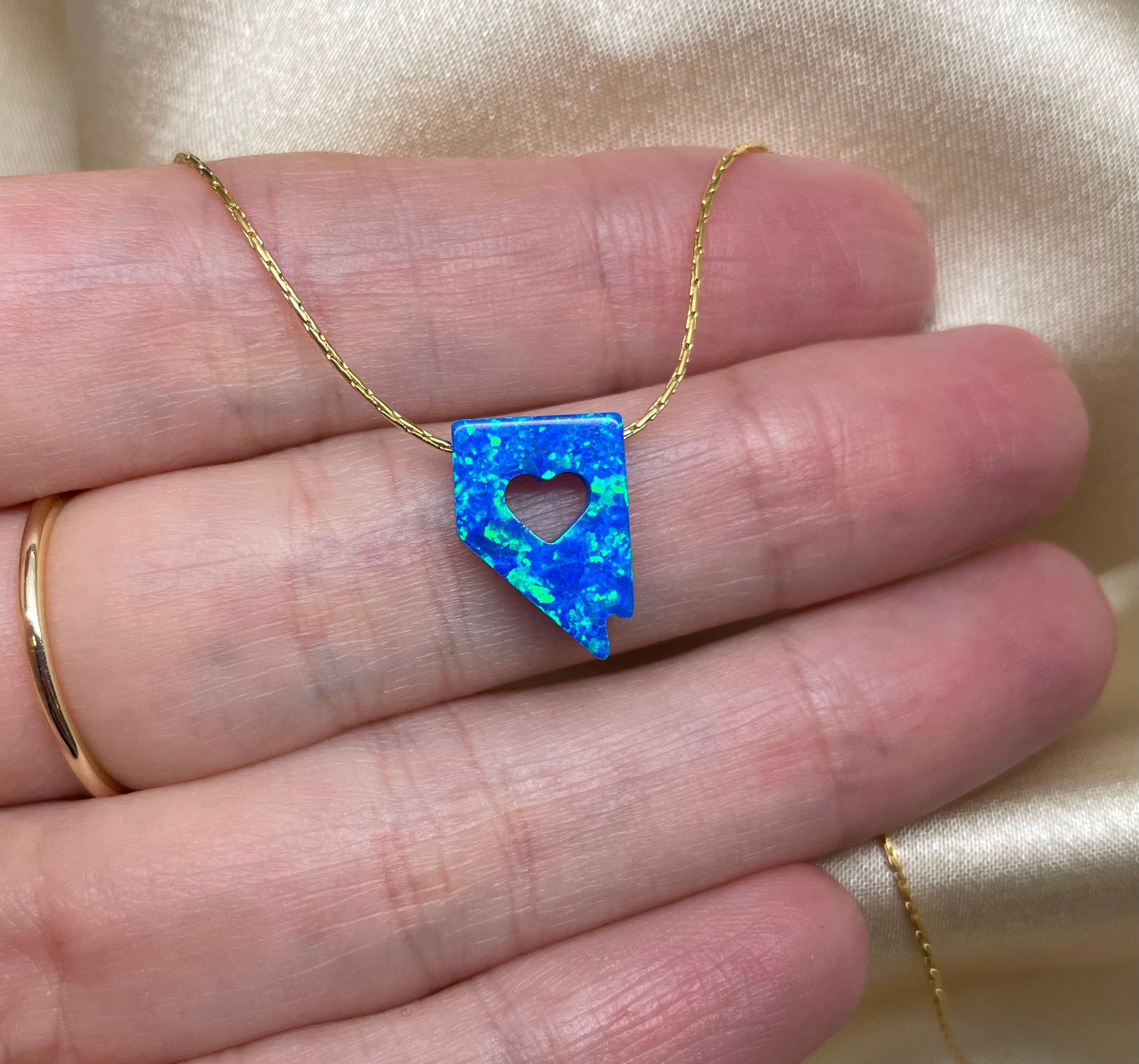 Blue opal necklace with heart cutout held between fingers against a beige background