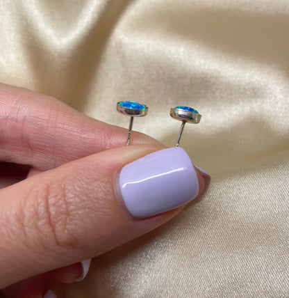 Small round earrings held between fingers against a beige fabric background
