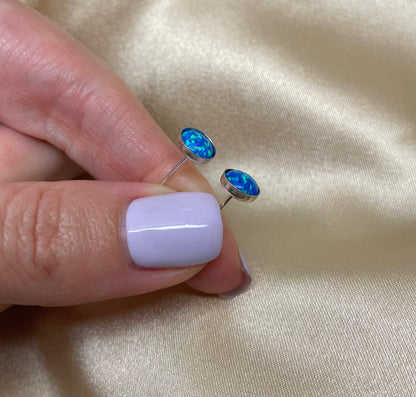 Blue opal stud earrings held between fingers with a beige fabric background