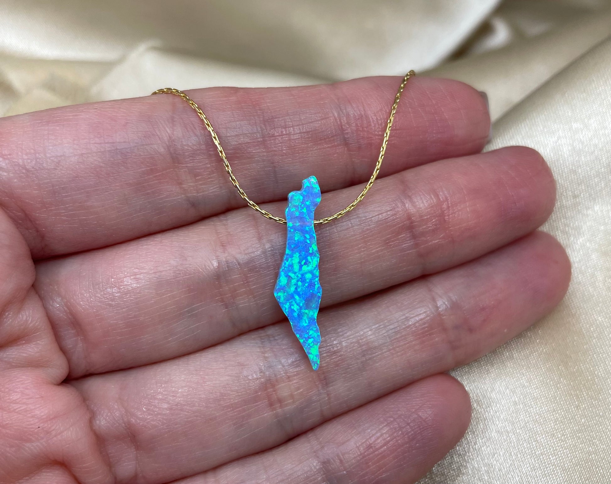 Opal pendant on a gold chain held in a hand against a beige fabric background