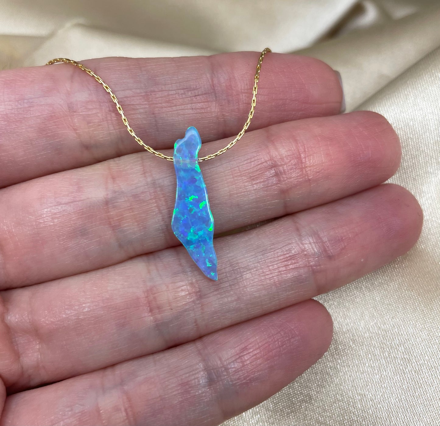 Opal pendant on a gold chain held in a hand against a neutral background