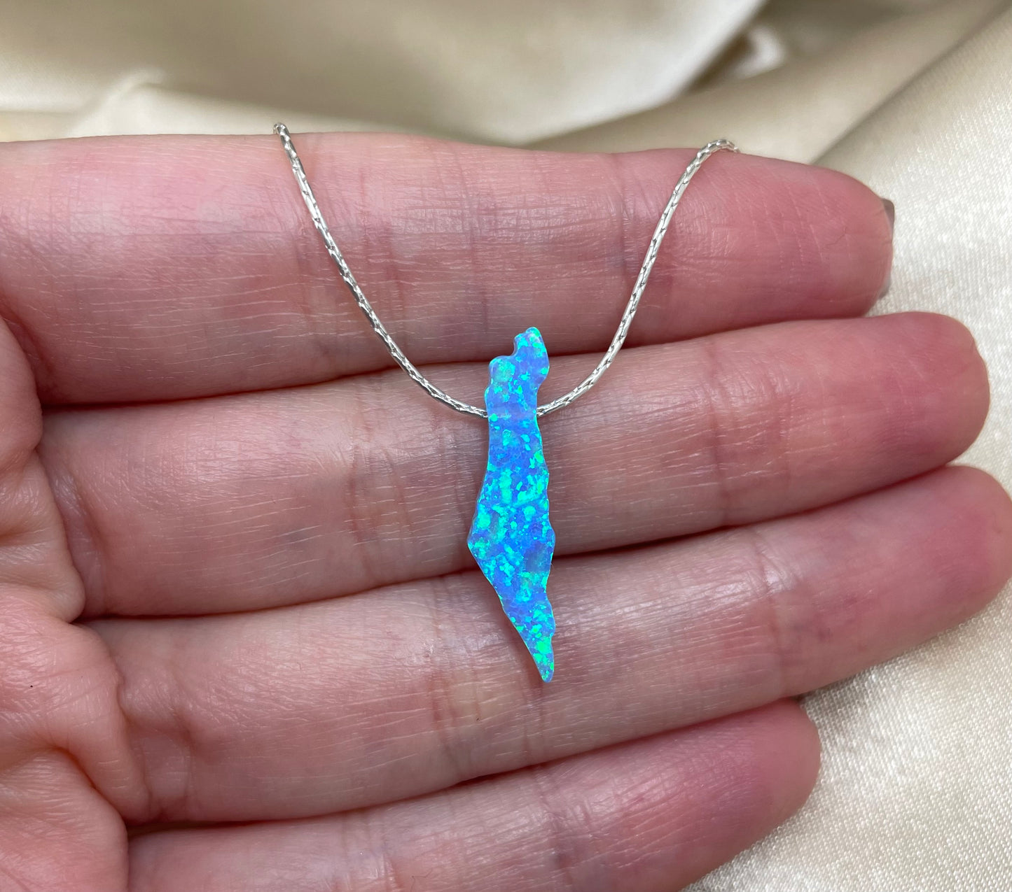 Blue opal pendant on a silver chain held in a hand against a neutral background