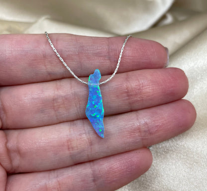 Blue opal pendant on a silver chain held in a hand against a beige fabric background