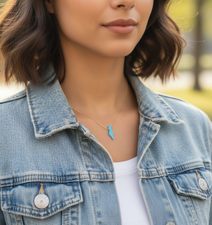 Person wearing a denim jacket with a necklace featuring a blue pendant.