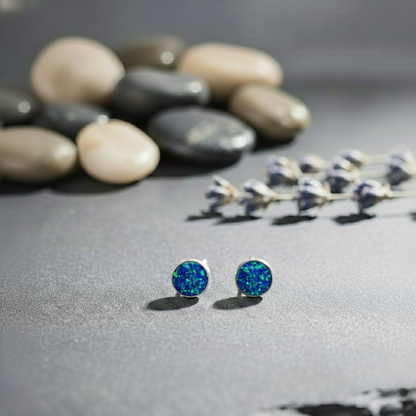 Blue opal stud earrings on a textured surface with stones and lavender in the background