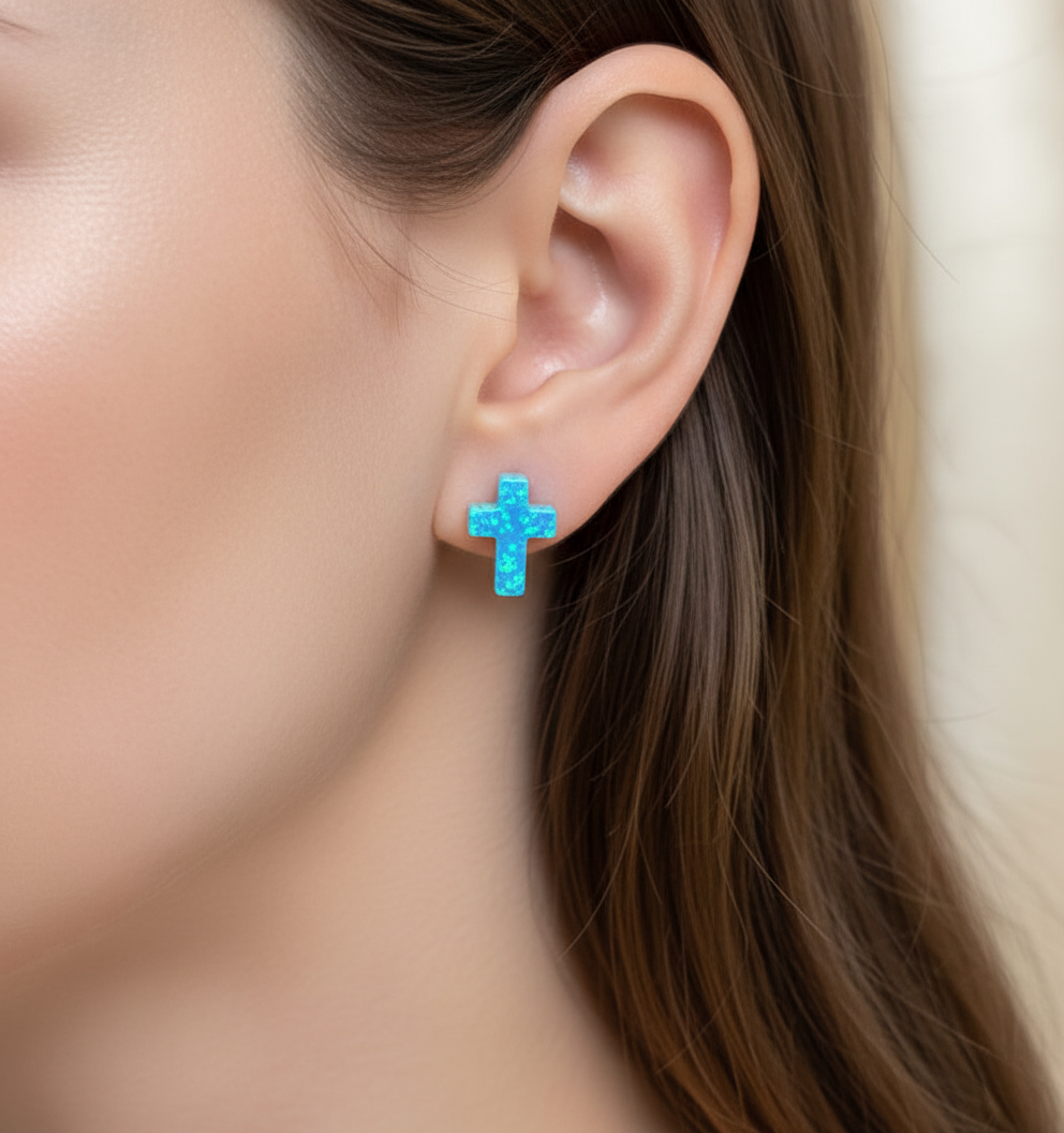 Close-up of an ear wearing a blue cross earring with blurred background