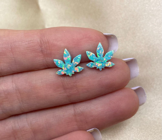 A pair of green opal marijuana leaf-shaped earrings on a person's ear, showcasing the design and color.